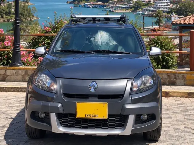 Renault Sandero gris oscuro de Latidos Tours, de frente, con barras de techo, junto al embalse de Guatapé