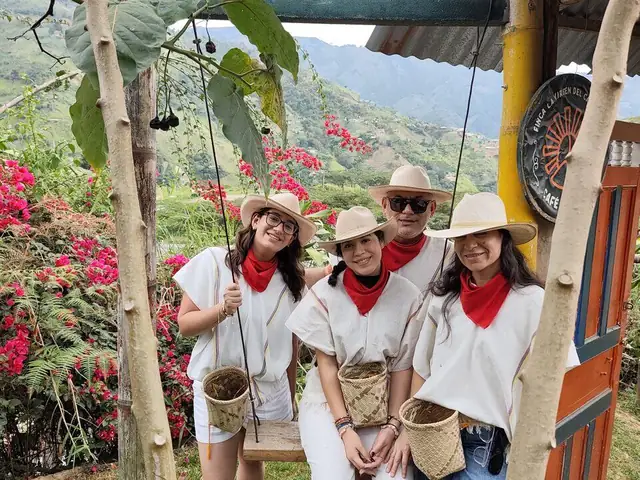 Visitantes con sombrero, poncho y canasto recolector en la finca cafetera, con las montañas de Antioquia al fondo